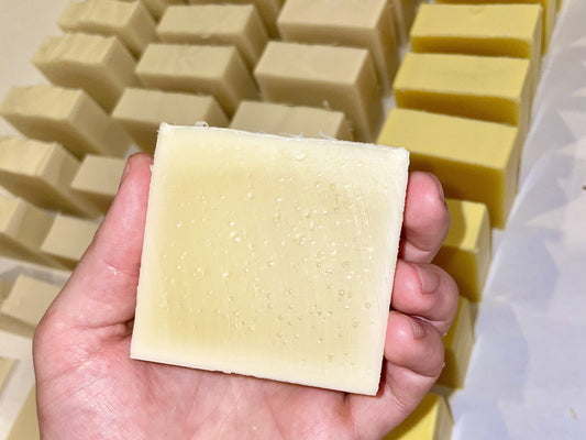 Hand holding a freshly cut cold process soap bar with multiple freshly cut soap bars stacked in the background