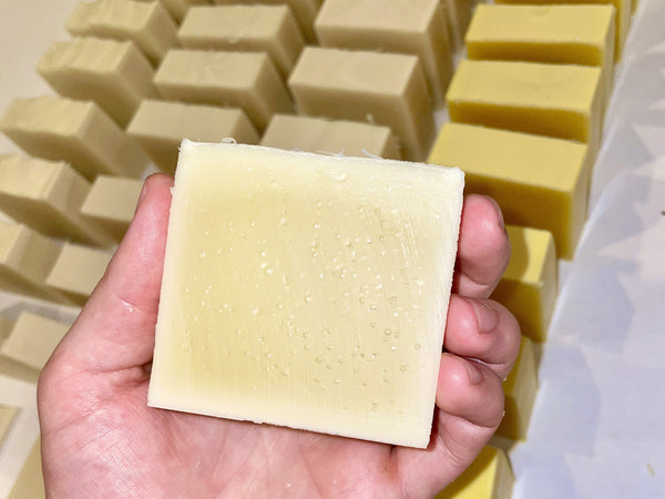 Hand holding a freshly cut cold process soap bar with multiple freshly cut soap bars stacked in the background